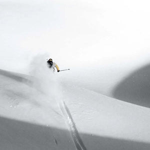 Skier in Arctic Volt gear carving through deep powder snow