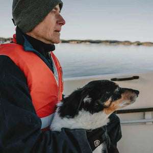 Man in a life vest holding a black and white dog on a boat