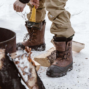 Person wearing brown Baffin winter boots standing in snow near firewood