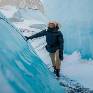 Person wearing a black parka and tan pants standing between blue glacier walls