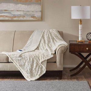 Cream faux fur heated throw blanket draped over a beige sofa