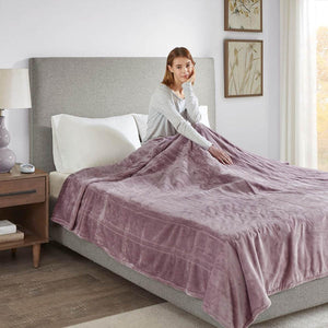 Woman sitting on a bed under a purple Beautyrest heated blanket
