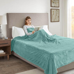 Person reading a book in bed covered by a teal Beautyrest plush blanket