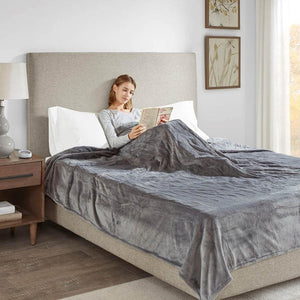 Person reading a book in bed under a grey Beautyrest heated blanket