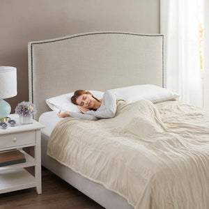 Person sleeping under a Beautyrest heated blanket on a bed with a beige upholstered headboard