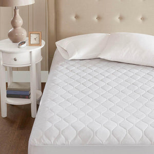 White quilted mattress protector on a bed with a bedside table