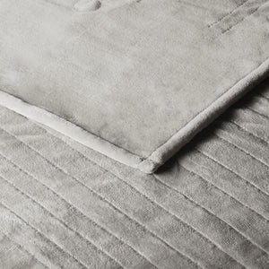 Close up of a grey velvet blanket with horizontal quilted stitching
