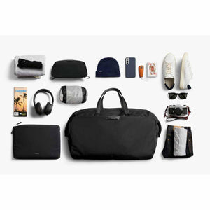 Bellroy black duffel bag surrounded by travel essentials including clothing, shoes, headphones, and camera