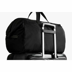 Bellroy black duffel bag secured to a rolling suitcase handle