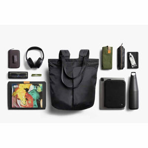 Bellroy black tote backpack surrounded by organized daily carry items including headphones tablet and water bottle