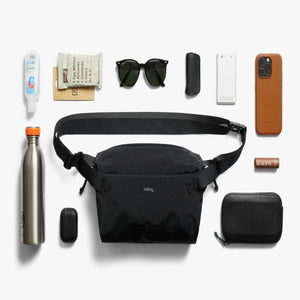 Bellroy black sling bag surrounded by everyday carry items including a water bottle sunglasses and phone case