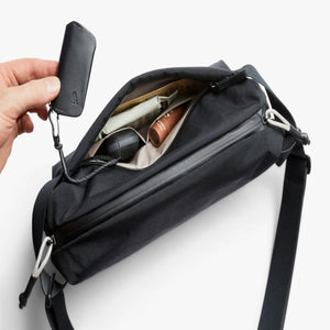 Hand holding a Bellroy key clip attached to the inside of an open black sling bag
