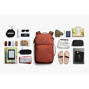 Bellroy backpack surrounded by travel accessories including clothing, passport, snacks, and electronics