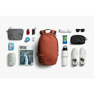Bellroy backpack surrounded by organized travel accessories and personal items on a white background