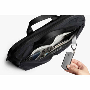 Hand holding a Bellroy key cover attached to a clip inside an open black briefcase
