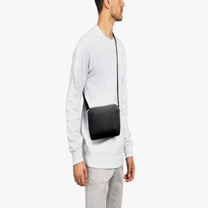 Person wearing a black Bellroy crossbody bag over a light grey sweater