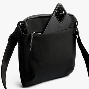 Black Bellroy crossbody bag with a smartphone partially inserted into the front zippered pocket