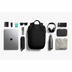 Bellroy black backpack surrounded by laptop, headphones, water bottle, and personal accessories on white background