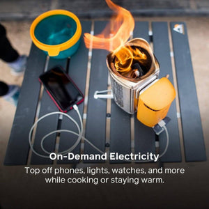 BioLite camp stove burning wood and charging a smartphone via USB cable on a folding table