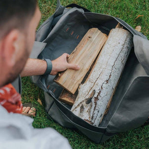 Person placing firewood into a grey BioLite gear bag on grass