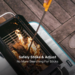 Hand using a BioLite fire poker to adjust burning wood in a portable grill