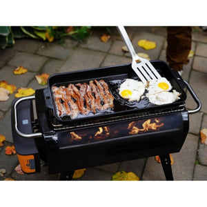Bacon and eggs cooking on a BioLite portable grill with a spatula