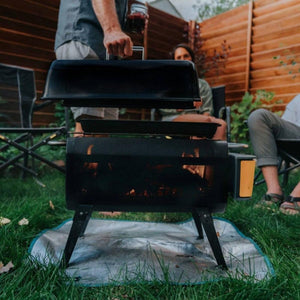 Person lifting the lid of a BioLite portable grill on a lawn
