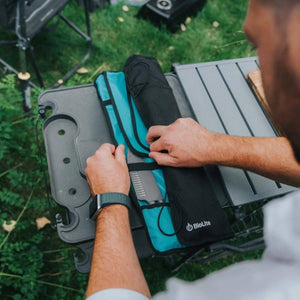 Person packing a BioLite camp stove into a teal and black storage bag on a folding table