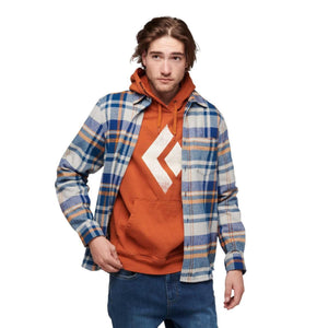 Man wearing a Black Diamond orange hoodie under a blue and tan plaid flannel shirt