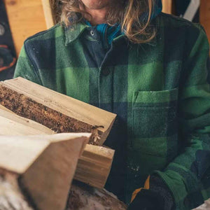 Person wearing a Black Diamond green and black plaid flannel shirt while carrying firewood