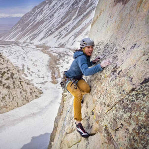 Climber wearing Black Diamond gear scaling a rock face above a snowy valley