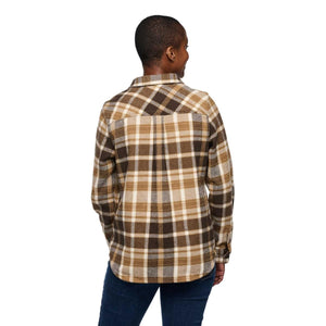 Back view of a person wearing a brown and tan plaid flannel shirt with blue jeans