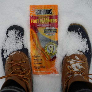 Hothands insole foot warmers package placed between two snow covered winter boots
