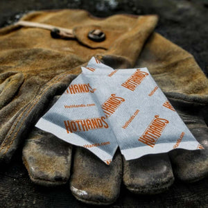 Two HotHands hand warmer packets resting on a brown leather work glove