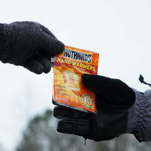 Two gloved hands holding a Hothands hand warmer packet