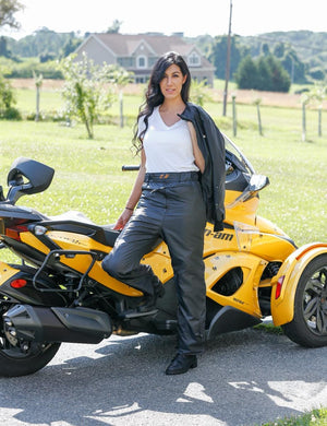 Woman wearing California Heat leather pants and white shirt standing by a yellow three-wheeled motorcycle
