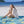 Woman sitting on a blue and yellow flamingo print beach towel on white sand