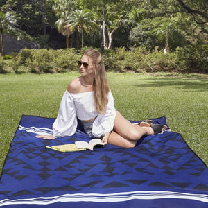 Woman sitting on a blue and black geometric patterned outdoor blanket in a park