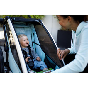 Child sitting in a light blue Thule bike trailer with a parent opening the mesh cover