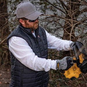 Person wearing a DeWalt black quilted vest and gloves while using a yellow power tool outdoors