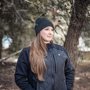 Woman wearing a black DeWalt heated jacket and beanie outdoors