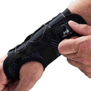 Hand adjusting a black wrist brace with a Boa dial closure system