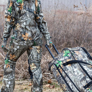 Person wearing DSG Outerwear camouflage hunting gear pulling a matching camouflage rolling duffel bag