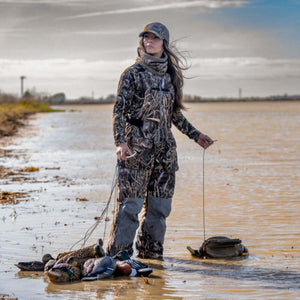 Woman wearing camouflage hunting gear standing in shallow water with duck decoys