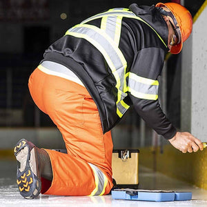 Worker in high visibility jacket and orange pants kneeling on ice while using tools