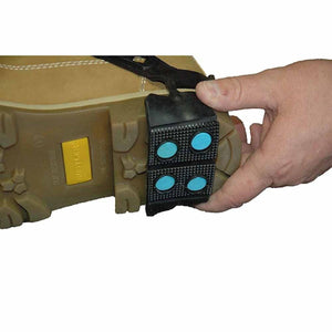 Hand applying a black rubber ice cleat with blue studs onto the sole of a tan work boot