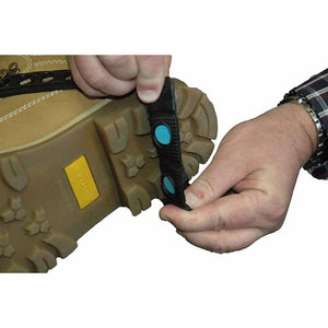 Hands attaching a black rubber ice cleat with blue studs to the sole of a tan work boot