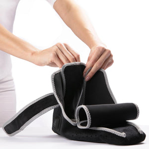Person adjusting a black HealthyLine heated ankle wrap with velcro straps