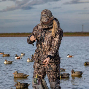 Woman wearing DSG Outerwear camouflage hunting gear standing in water with duck decoys