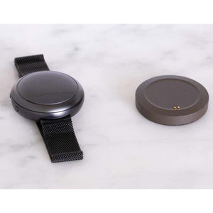 Embr Wave wearable device with black mesh strap and circular charging dock on white marble surface